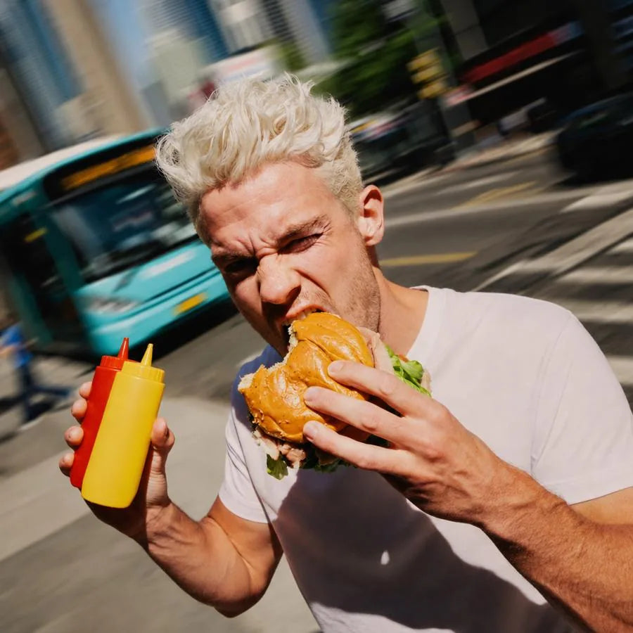 Man taking a big bite of a burger while walking fast down a city street