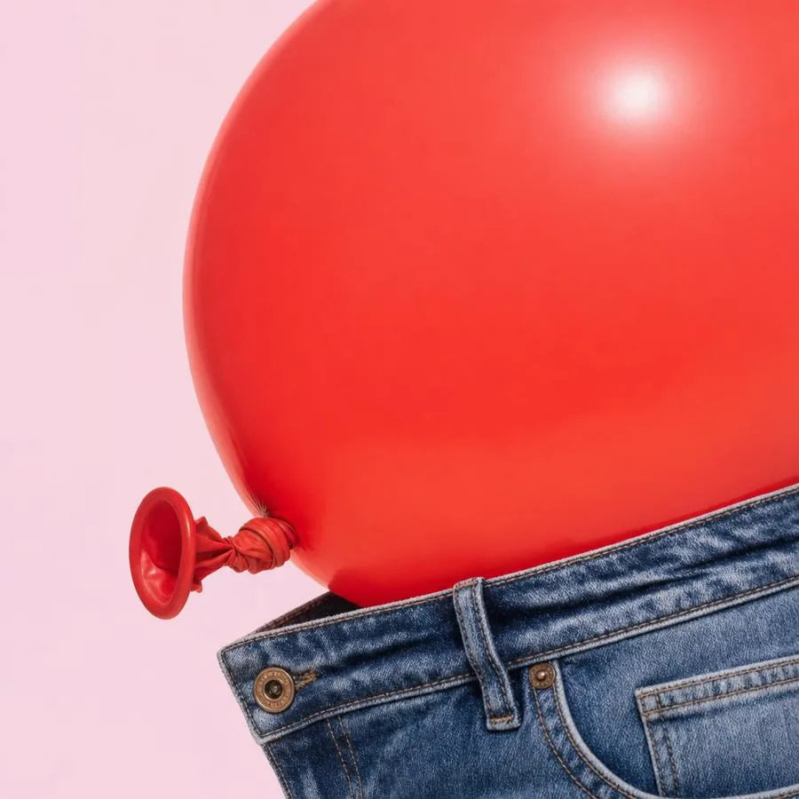 Red balloon pressing out of the waistband of jeans, showing a bloated stomach
